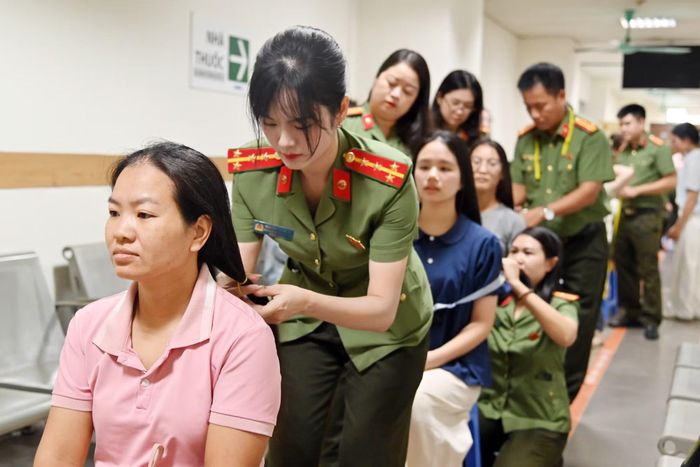 Hàng ghế nối dài theo vạch sơn chỉ đường. Sau lưng mỗi người hiến tóc là một chiến sĩ công an.