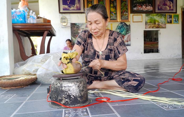  Người thợ dùng ấm nhôm và tấm gang nóng ép, chuốt lá kè mỡ tạo phẳng trước khi kết lá làm nón 