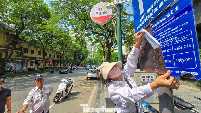 Ôtô đỗ tại điểm trông giữ trên phố Lý Thường Kiệt, một trong 12 tuyến phố áp dụng mức giá mới. Nhân viên điểm trông giữ xe đang thay đổi bảng giá mới theo quy định.