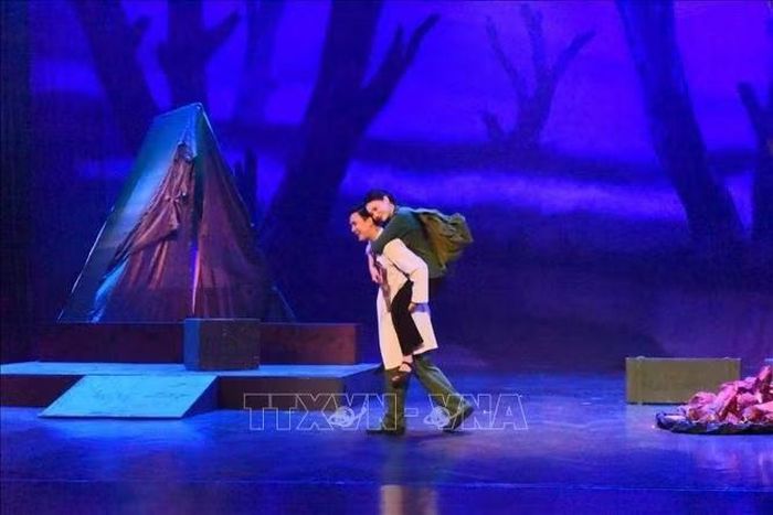 Bác sĩ Quân y cõng người phụ nữ bị thương nặng khi xông pha cứu học trò khỏi làn bom đạn trong vở kịch "Người con gái Hà Nội". Ảnh: Tuyết Mai/TTXVN