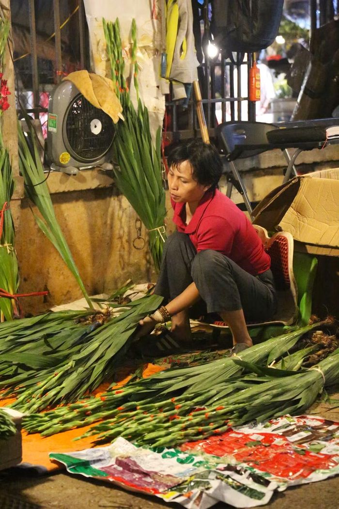 Dưới ánh đèn rủ, tiểu thương tỉ mỉ tuốt lá, phân loại những cành hoa dơn xanh mướt trước khi xếp thành từng bó ngăn nắp