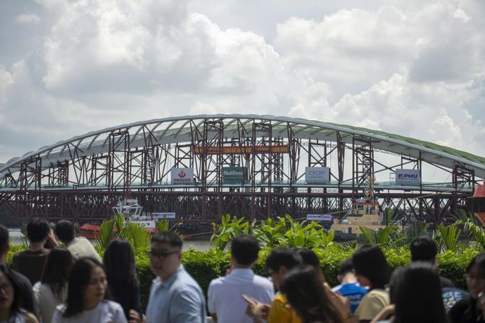 Hình ảnh vòm thép lá dừa nước chậm rãi tiến về trung tâm thu hút sự chú ý của người dân, tạo nên không khí háo hức trên bờ. Một số người tranh thủ lưu lại khoảnh khắc nhịp cầu tương lai được đưa về thành phố.