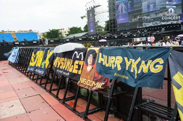 Dọc hàng rào khu khán giả, băng rôn của các fandom được treo nối tiếp, với những cái tên như Hurrykng, Jaysonlei, Dương Domic... Người hâm mộ tìm khoảng trống dễ nhìn từ sân khấu để đặt bảng tên, tìm cơ hội tương tác cùng idol ở concert quy tụ hàng chục nghìn người.