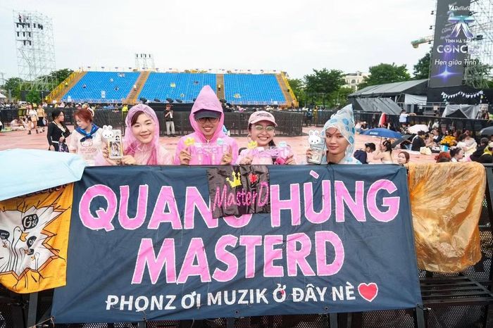 Fan Quang Hùng MasterD mặc áo mưa, đứng sau băng rôn mang tên nam ca sĩ. Nhóm khán giả đến xếp hàng trước vài giờ đồng hồ, mang theo đồ dùng và vật dụng cổ vũ để chờ chương trình bắt đầu lúc 19h.