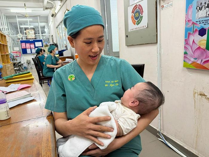 Bận rộn hỗ trợ các đồng nghiệp nhưng điều dưỡng Phan Ngọc Cơ vẫn ôm theo bé gái bị bỏ rơi. Trong vòng tay "người mẹ", đứa bé nhoẻn miệng cười. Ảnh: Thanh Huyền