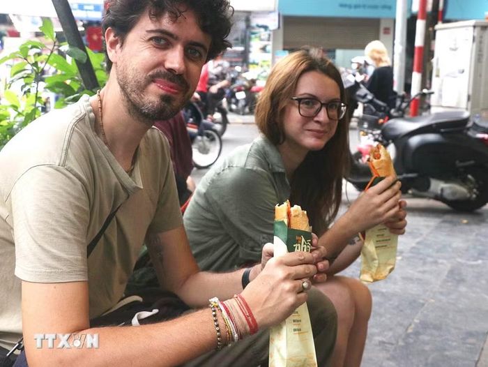 Khách du lịch nước ngoài thưởng thức món bánh mỳ trên đường phố Hà Nội. (Ảnh: TTXVN)