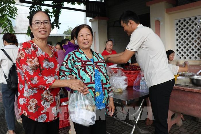 Cô Lâm Thị Cúc Huỳnh (trái) trao tặng các suất ăn cho người dân có hoàn cảnh khó khăn. Ảnh: Thanh Hòa - TTXVN