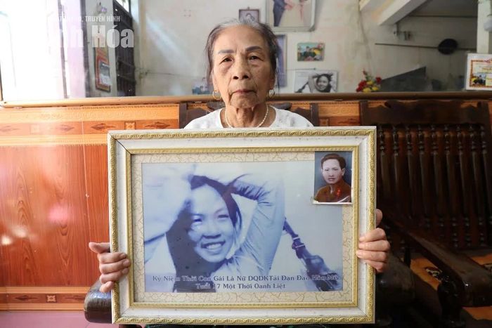 Bà Hoàng Thị Thá, nguyên Tiểu đội trưởng Tiểu đội nữ du kích tải đạn tiếp tế cho đảo Hòn Mê bên bức ảnh chụp mình thời con gái.