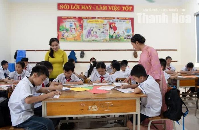 Cô giáo hướng dẫn học sinh làm thiệp và viết lời chúc mừng tại lớp học.