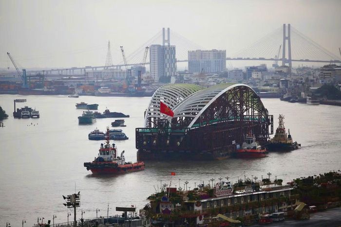 Khoảng 10h23, siêu sà lan chở vòm thép tiến qua cầu Phú Mỹ. Các tàu trong đoàn liên tục phát còi cảnh báo khi di chuyển. Đến khoảng 10h30, đoàn lai dắt vượt qua khu vực cầu, tiếp tục xuôi theo luồng sông hướng về trung tâm thành phố.