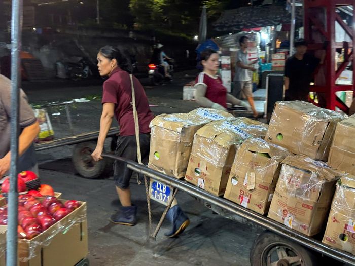 Đôi chân vững vàng, đôi tay chắc khỏe, người phụ nữ cần mẫn kéo xe hàng qua khu chợ, thể hiện sức bền và sự dẻo dai của người lao động.