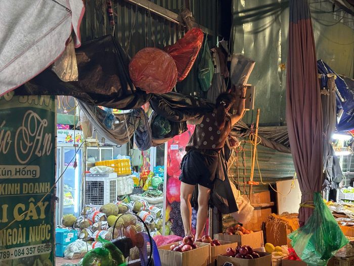 Giữa những thùng hoa quả chất đầy, người phụ nữ khéo léo sắp xếp hàng hóa, khép lại câu chuyện về những đôi tay cần mẫn làm nên vẻ đẹp bình dị của lao động.