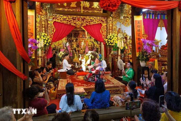 Toàn cảnh không gian thực hành nghi lễ hầu đồng tại đình Đông Thành, với thanh đồng thực hiện các động tác diễn xướng trước ban thờ, bên cạnh những người phụ lễ và đông đảo người dân tham dự. (Ảnh: Phạm Tuấn Anh/TTXVN)