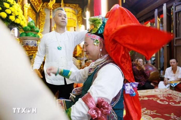 Người phụ lễ hỗ trợ thanh đồng trong quá trình thay đổi, điều chỉnh trang phục khi thực hành nghi lễ hầu đồng tại đền Hàng Vải. Bên cạnh thanh đồng và các cung văn, những người phụ lễ giữ vai trò hỗ trợ chuẩn bị khăn áo, vật phẩm và phối hợp thực hiện các công đoạn nghi lễ. Sự tham gia của nhiều thành viên thể hiện tính cộng đồng trong thực hành tín ngưỡng, nơi những kiến thức và kỹ năng truyền thống được duy trì thông qua hoạt động thực hành. (Ảnh: Phạm Tuấn Anh/TTXVN)