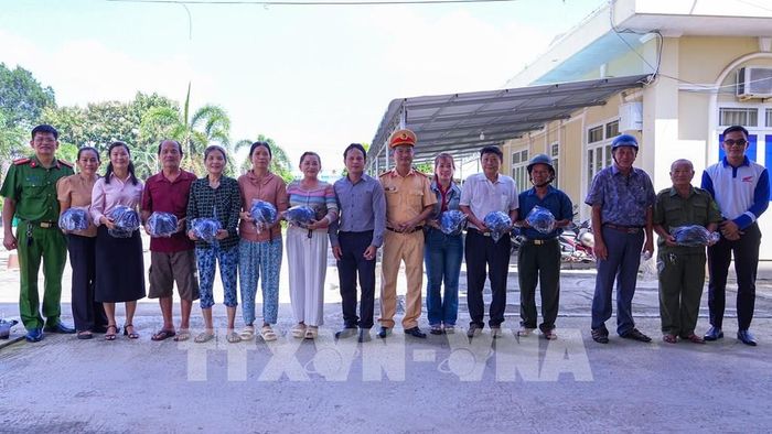 Đại diện lực lượng chức năng, chính quyền địa phương tặng mũ bảo hiểm cho người dân tham gia chương trình. Ảnh: Minh Phú - TTXVN