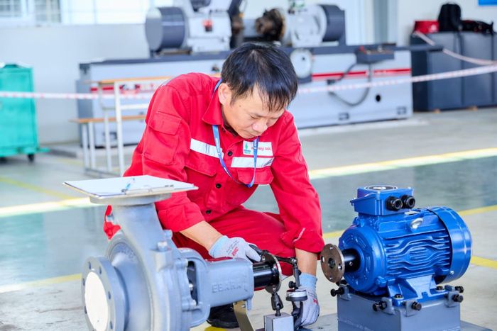 Thí sinh sử dụng đồng hồ so để kiểm tra độ đồng tâm, đánh giá độ lệch giữa trục động cơ điện và trục bơm ly tâm. Đây là công đoạn quan trọng trong quá trình căn chỉnh đồng trục, đòi hỏi người thợ phải thực hiện chính xác các thao tác đo đạc, ghi nhận thông số và xác định mức độ sai lệch so với yêu cầu kỹ thuật. Nếu hai trục không được căn chỉnh phù hợp, thiết bị có thể phát sinh rung động, tiếng ồn, gia tăng tải trọng lên ổ đỡ và khớp nối, từ đó ảnh hưởng đến tuổi thọ cũng như hiệu quả vận hành của hệ thống.