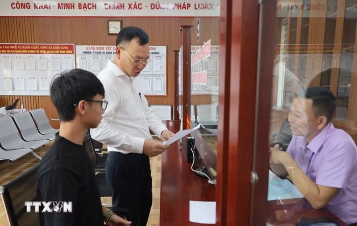 Ông Phạm Văn Định, Chủ tịch Ủy ban Nhân dân xã Kiến Hưng (người đứng) trò chuyện với người dân đến làm dịch vụ công tại xã. (Ảnh: Minh Thu/TTXVN)