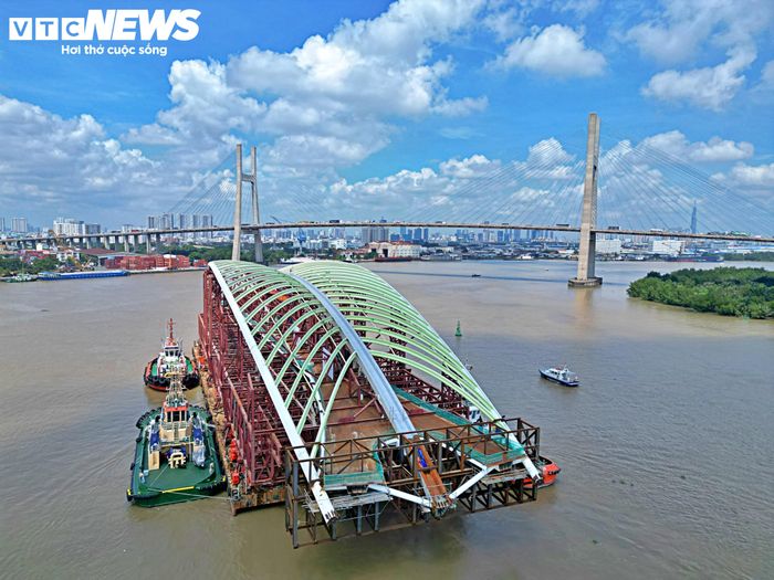 Tổ hợp kết cấu được lai dắt từ Vũng Tàu về TP.HCM có tổng trọng lượng khoảng 3.400 tấn, gồm nhịp chính vòm thép dài 187 m, nặng 1.400 tấn và hệ khung đỡ chuyên dụng nặng khoảng 2.000 tấn. Hiện sà lan chở kết cấu này neo dọc bờ sông phía Thủ Thiêm, chờ đưa vào vị trí lắp đặt.