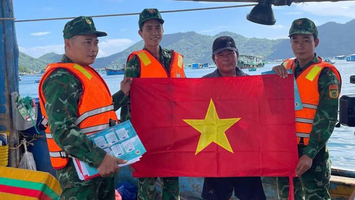 Cán bộ, chiến sĩ Đồn Biên phòng Cửa khẩu cảng Vũng Rô trao cờ Tổ quốc và tuyên truyền, vận động ngư dân chấp hành nghiêm các quy định về chống khai thác IUU. (Ảnh: NGUYỄN LÂN)