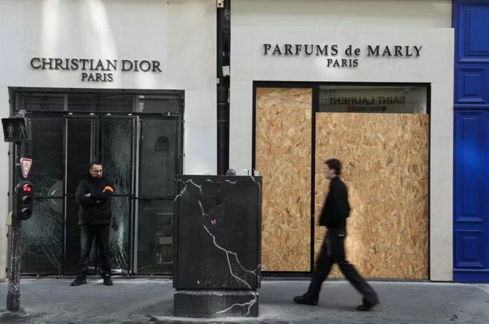 Một nhân viên bảo vệ đứng canh gác tại cửa hàng Dior bị phá hủy ở Paris hôm 18/10. Ảnh: Reuters.