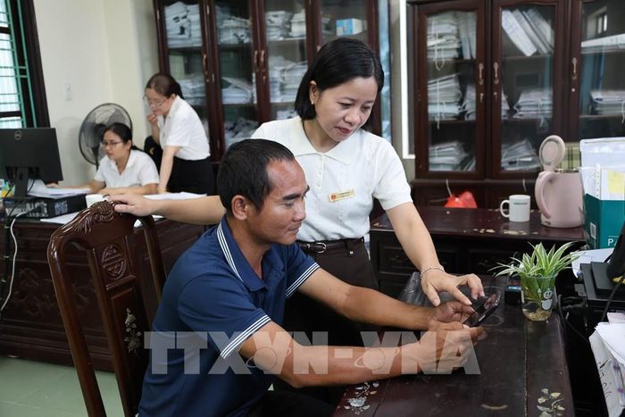 Cán bộ Thuế Cơ sở 9 tỉnh Hưng Yên hướng dẫn hộ kinh doanh cài đặt ứng dụng thuế điện tử Etax Mobile. Ảnh: Thu Hoài - TTXVN