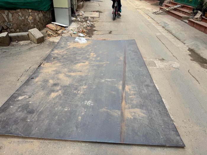 Mặt đường bị hư hỏng đang được che đậy tạm bằng tấm sắt cỡ lớn