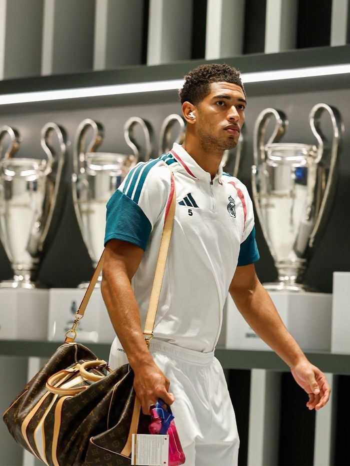Real Madrid kết hợp cùng Louis Vuitton trong những tạo hình mang tinh thần thể thao đương đại tại trận đấu ngày 22/10. Áo khoác thể thao trắng phối xanh cổ vịt, điểm các đường sọc đặc trưng của adidas và chi tiết đỏ, đi cùng quần đồng bộ. Túi du lịch họa tiết monogram nâu kinh điển của Louis Vuitton trở thành điểm nhấn, kết nối trang phục năng động với dấu ấn xa xỉ của nhà mốt Pháp. Ảnh: Real Madrid.