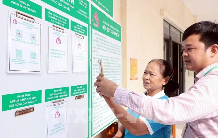 Cán bộ NHCSXH Lục Nam hướng dẫn tổ trưởng tổ tiết kiệm tra cứu các chương trình vay vốn trên ứng dụng VBSP SmartBanking. Ảnh: Trần Việt - TTXVN