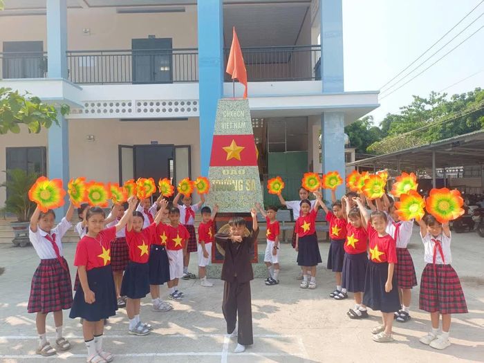 Học sinh Trường Tiểu học Khánh Bình - Phân hiệu Khánh Đông bên mô hình cột mốc Trường Sa trong khuôn viên trường.