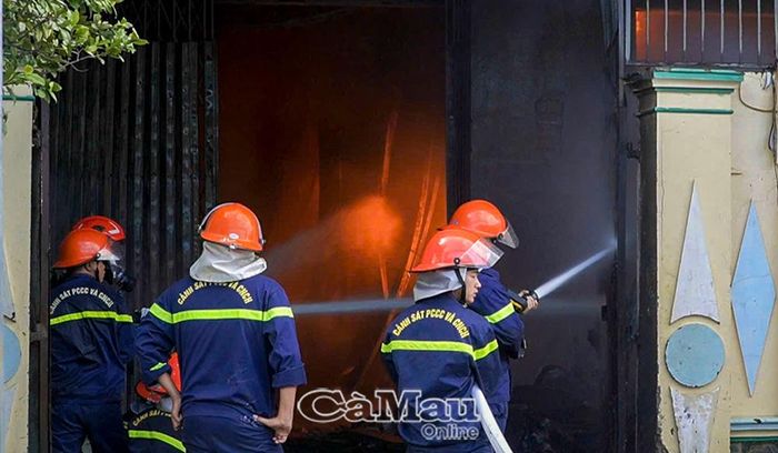 Lực lượng chức năng tiếp cận sát cửa nhà kho, phun nước áp lực cao để dập tắt lửa bên trong.