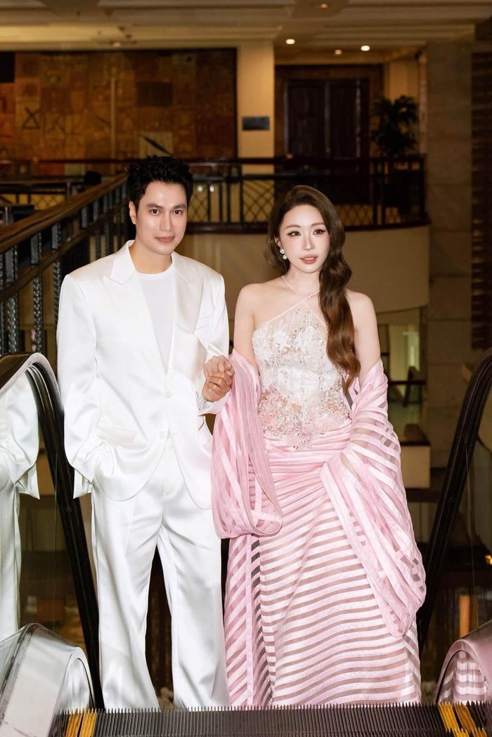Việt Anh diện bộ vest trắng kết hợp áo thun cùng tông màu. Trong khi đó, Quỳnh Nga nổi bật với đầm dạ hội ôm sát, đính đá lấp lánh ở phần thân trên, kết hợp thiết kế trễ vai và khăn choàng dài màu hồng với những đường kẻ ngang.