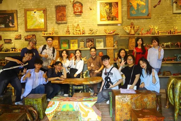 Nghệ nhân Nguyễn Tấn Phát (giữa) chụp hình cùng các bạn trẻ tham quan, trải nghiệm không gian sơn mài tại làng cổ Đường Lâm, Sơn Tây, Hà Nội. Ảnh: FBNV