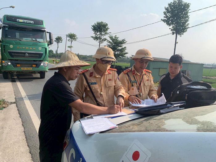 Cán bộ Đội Cảnh sát giao thông đường bộ số 9 hướng dẫn tài xế ký biên bản. Ảnh: PV
