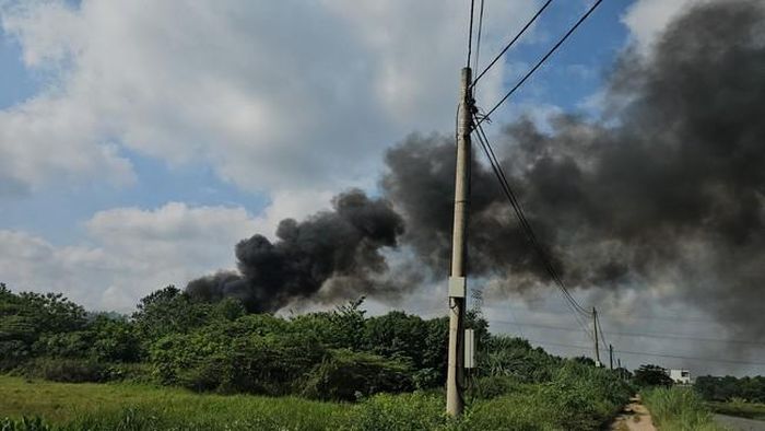 Cột khói đen dày đặc bao trùm một góc khu vực có nhiều cây xanh, gần đường giao thông và hệ thống đường dây điện - (ảnh Nhật Tân).