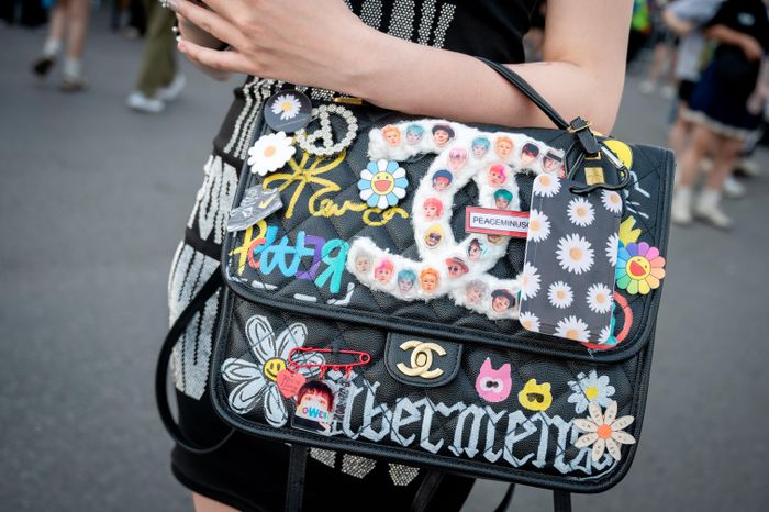  Trong khi đó, chiếc túi Chanel của Liu Fen (31 tuổi, Trung Quốc) dễ khiến người qua đường phải ngoái nhìn bởi loạt chi tiết được cá nhân hóa theo cảm hứng từ G-Dragon. Trên nền túi đen, cô sắp đặt tên album Übermensch, họa tiết hoa cúc đặc trưng, hình ảnh các thành viên, sticker và những dòng chữ nhiều màu sắc. Món phụ kiện hàng hiệu vì thế trở thành nơi Liu Fen thể hiện tình yêu với nhóm, đồng thời cho thấy sự sáng tạo của người hâm mộ trong cách biến đồ dùng cá nhân thành dấu ấn riêng. 