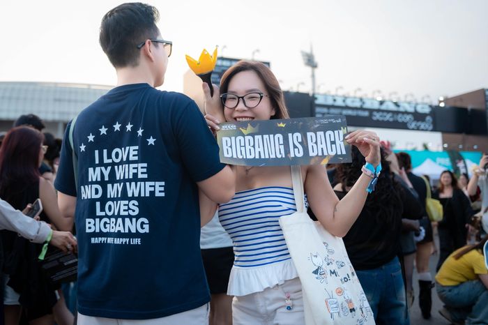  Một cặp đôi mang đến khoảnh khắc vui nhộn trước giờ concert. Trong khi người vợ diện áo quây kẻ xanh trắng, cầm lightstick và tấm bảng “BIGBANG IS BACK”, chiếc áo phông của người chồng lại gây chú ý với dòng chữ hài hước: “I love my wife and my wife loves BigBang” (Tôi yêu vợ tôi và vợ tôi yêu BigBang). Màn “bắt trend” dí dỏm vừa thể hiện sự ủng hộ của người chồng với sở thích của vợ, vừa cho thấy sức hút của concert có thể trở thành chất liệu gắn kết những câu chuyện đời thường. 