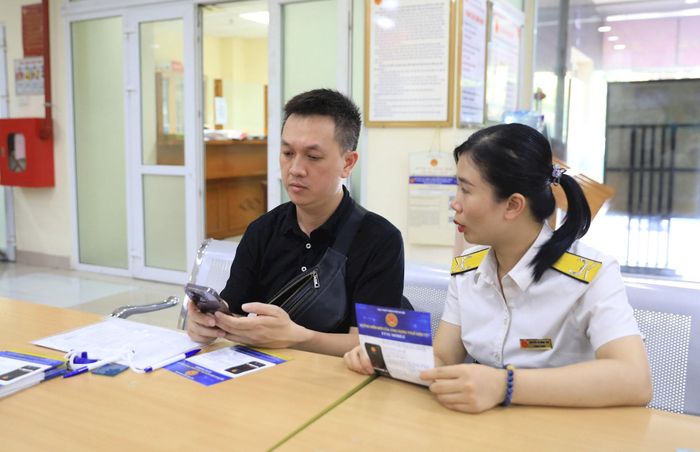 Cán bộ Thuế hướng dẫn người dân sử dụng ứng dụng eTax-Mobile để tra cứu thông tin, nộp thuế. Ảnh: Nguyễn Quang