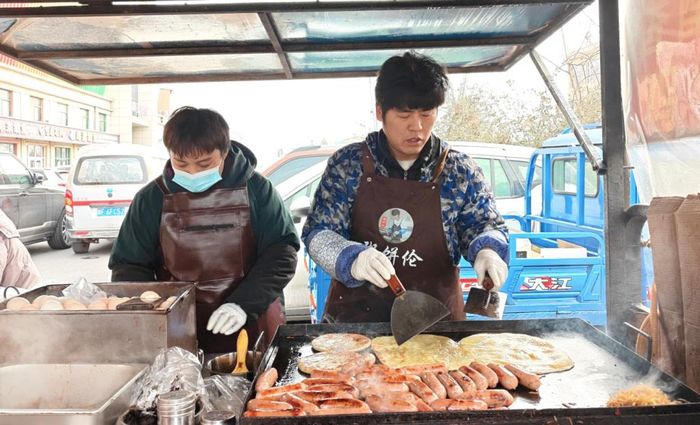  Bai Xianying (bên phải) cùng vợ làm bánh bán bên ngoài trung tâm thương mại dệt may Lương Mã Đài ở Bảo Định (tỉnh Hà Bắc, Trung Quốc, tháng 2/2026. Ảnh: Cheng Ting/Sixth Tone. 