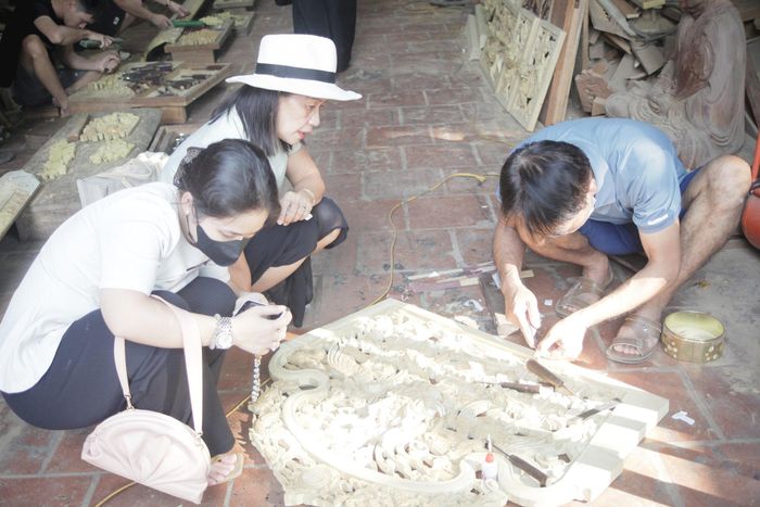 Du khách tìm hiểu kỹ thuật chạm khắc gỗ truyền thống tại một cơ sở sản xuất ở làng nghề Sơn Đồng. Ảnh: PV