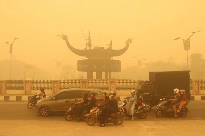 Người dân đi xe máy đeo khẩu trang di chuyển giữa làn khói dày đặc do cháy rừng và cháy đất than bùn ở Palangkaraya, Trung Kalimantan vào ngày 24-10-2026