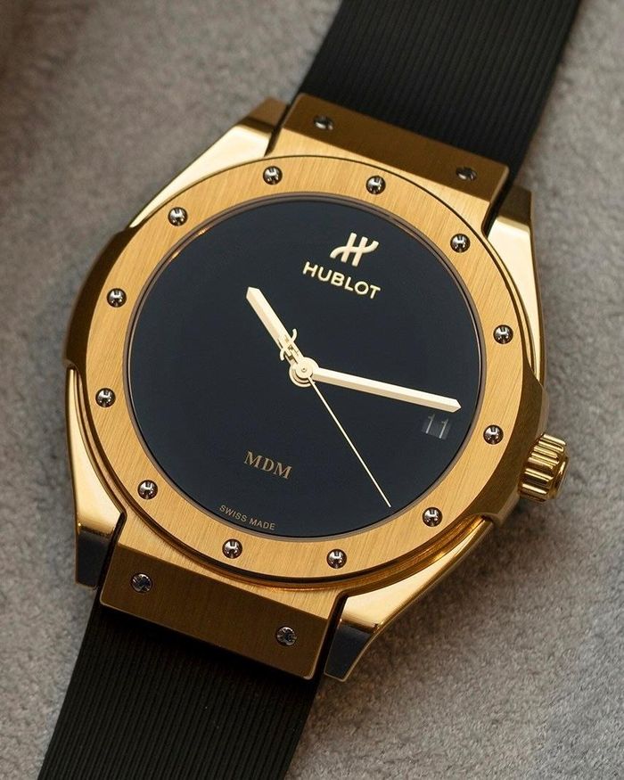 Kylian Mbappé (1998) xếp thứ hai trong cuộc đua Quả bóng vàng nam 2026, sau Harry Kane. Tiền đạo Real Madrid chọn Hublot Classic Fusion Tributo 38 mm bằng vàng 18K. Mẫu đồng hồ gợi lại thiết kế Hublot ra đời năm 1980, với mặt số đen tối giản, không có cọc số và 12 vít trên vành bezel. Bên trong là bộ máy tự động HUB1711, có thời gian dự trữ năng lượng khoảng 50 giờ. Giá thị trường của đồng hồ vào khoảng 30.900 USD. Ảnh: Matthew Childs/Reuters, SJX Watches.