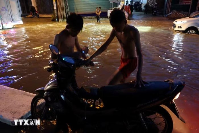Các em nhỏ sống ở đường Nguyễn Bình hỗ trợ người đi đường có xe chết máy do triều cường. (Ảnh: Hồng Đạt/TTXVN)
