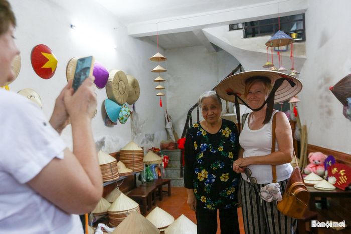 Những du khách quốc tế thích thú chụp ảnh cùng chiếc nón lá và người nghệ nhân tại không gian sản xuất nón Phú Mỹ.