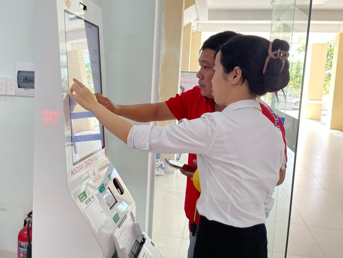 Cán bộ hướng dẫn người dân nộp hồ sơ trực tuyến tại thiết bị Kiosk. Ảnh: Lê Bằng