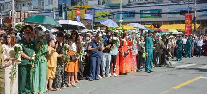 Người dân tay cầm nhành hoa trắng, đứng đợi dưới trời nắng nóng để tiễn đưa các anh hùng liệt sĩ - Ảnh: Quảng Đạo 