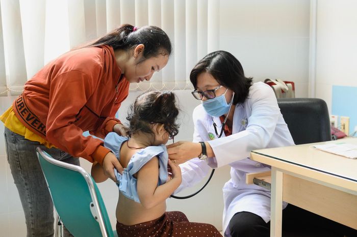 Bác sĩ nghe phổi cho một bệnh nhi có người nhà đi cùng. Với trẻ có biểu hiện ho, sốt hay khó thở, nghe phổi giúp bác sĩ sớm nhận ra những dấu hiệu bất thường ở đường hô hấp. Mỗi trẻ đều được phân loại, khám sàng lọc trước khi bác sĩ đưa ra chẩn đoán và hướng điều trị.