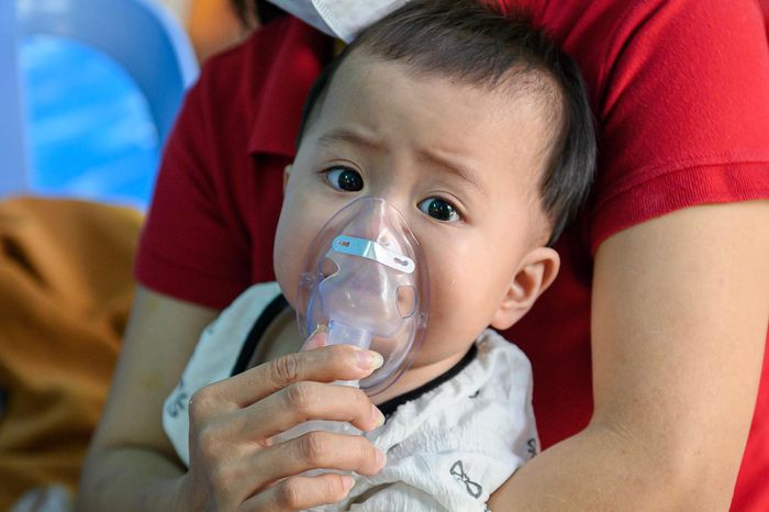 Một bệnh nhi nhỏ tuổi đang được người thân ôm vào lòng và hỗ trợ đeo mặt nạ thở khí dung. Trẻ nhỏ dưới 3 tháng tuổi và trẻ chưa hoàn thiện hệ miễn dịch là những đối tượng rất dễ chuyển nặng khi mắc các bệnh lý hô hấp mùa này.