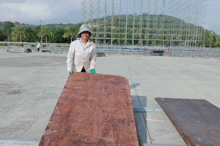 Nữ công nhân chuyển từng tấm ván để ghép sàn khán đài. Những dãy bậc dần thành hình trên hệ khung kim loại, trong khi vật tư vẫn được tập kết xung quanh để phục vụ thi công.