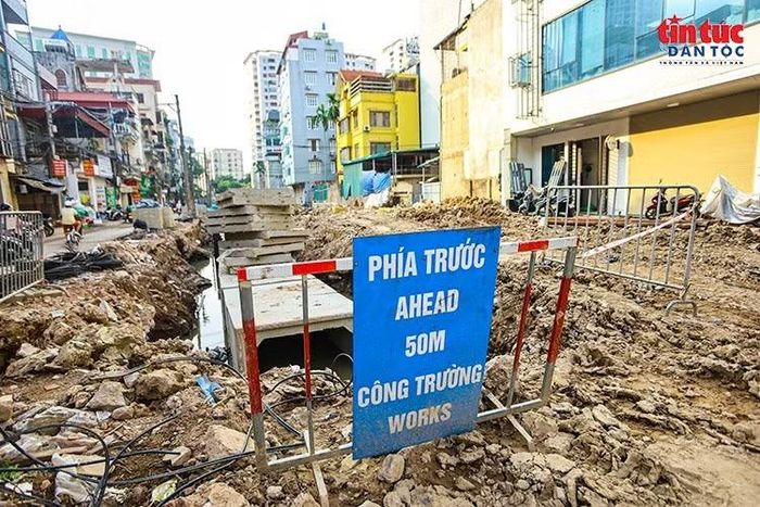 Biển cảnh báo công trường được đặt tại khu vực thi công cống thoát nước, nơi mặt đường đang đào sâu và chưa hoàn thiện.