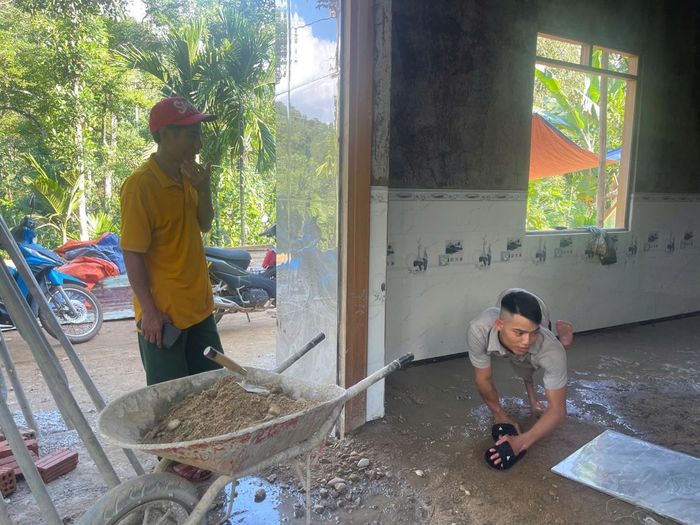 Anh Hồ Văn Quênh đang phụ giúp thợ lót gạch nền nhà khi chúng tôi đến thăm.